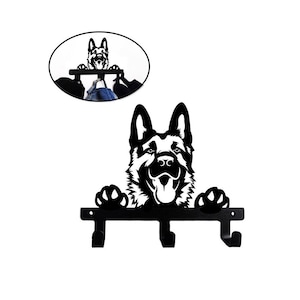 Puede incluir: Gancho de pared de metal negro en forma de silueta de cabeza de pastor alemán con tres ganchos. El perro sonríe con la lengua fuera.