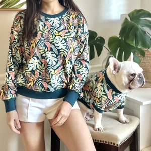 K&ouml;nnte beinhalten: Eine Frau und ein Hund tragen passende gr&uuml;ne und gelbe Hemden mit tropischem Muster. Die Frau tr&auml;gt wei&szlig;e Shorts und der Hund ist ein Franz&ouml;sischer Bulldogge.