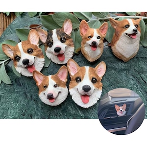 Puede incluir: Seis adornos de cerámica para coche en forma de corgi con diferentes expresiones. Los adornos están colocados sobre una superficie de mármol verde. Un adorno se muestra en una rejilla de ventilación de un coche.