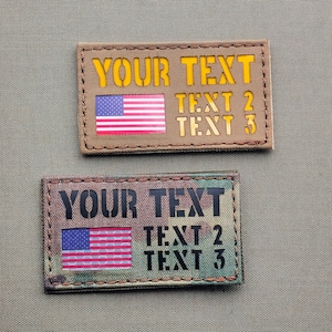 Può includere: Due toppe rettangolari con una bandiera americana e il testo "YOUR TEXT", "TEXT 2" e "TEXT 3". La toppa superiore è di colore beige con testo giallo e la toppa inferiore è mimetica con testo nero.