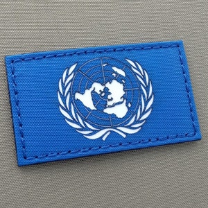 Könnte beinhalten: Ein blauer Patch mit einer weißen Umrandung des UN-Logos, das eine Weltkarte zeigt, die von Olivenzweigen umgeben ist.