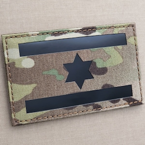 May include: A black and white Israeli flag patch with a six-pointed star in the center. The patch is made of a camouflage fabric and has a brown stitched border.
