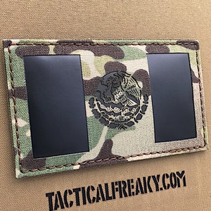 May include: A black and green camouflage fabric patch with the Mexican flag design. The flag features a black eagle with a snake in its talons, surrounded by a wreath of cacti. The patch has a black border and is stitched with brown thread. The text "TACTICALFREAKY.COM" is printed below the patch.
