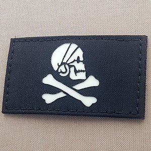May include: A black fabric patch with a white skull and crossbones design. The skull is wearing a white bandana.