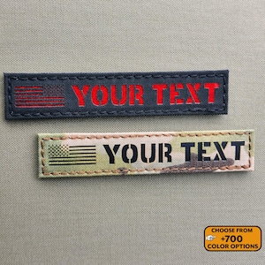 May include: Two rectangular patches with the text "YOUR TEXT". The top patch is navy blue with a red American flag and red text. The bottom patch is camouflage with a black American flag and black text. A small orange rectangle at the bottom right says "CHOOSE FROM +700 COLOR OPTIONS".