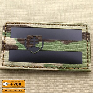 Pode incluir: Um remendo de camuflagem preto e verde com um emblema branco e preto. O remendo é costurado em um fundo de tecido bege. O texto no remendo diz "Escolha entre +700 opções de cores". O texto abaixo do remendo diz "Modelo mostrado: Multicam, IR".