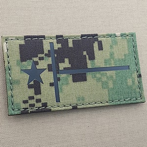May include: A black and green camouflage fabric patch with a black star and a black horizontal bar. The patch has a stitched border.