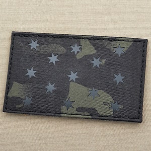 May include: A black and green camouflage patch with 13 black stars. The patch is made of a durable fabric and has a stitched edge.