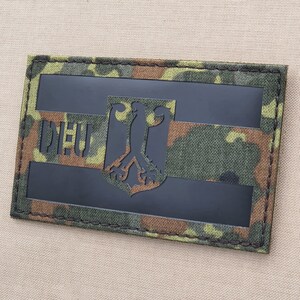 May include: A black and green camouflage fabric patch with a black German eagle and the text "DEU" in white.