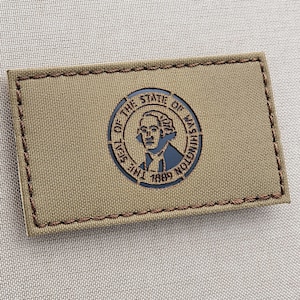 May include: A brown fabric patch with a black embroidered seal of the State of Washington. The seal features a portrait of George Washington and the text "The Seal of the State of Washington 1889".