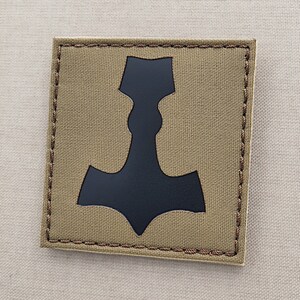 May include: A tan fabric patch with a black silhouette of a hammer, a symbol of strength and power.