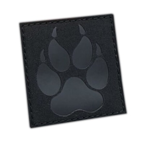 Pode incluir: Patch preto com a forma de uma pegada de pata com uma borda costurada. O patch é feito de um tecido preto com uma superfície texturizada.