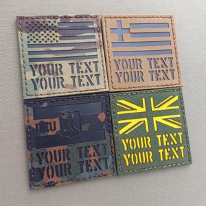 Può includere: Quattro toppe ricamate con diverse bandiere. Le toppe sono realizzate in tessuto mimetico di colore nero, verde e marrone. Le bandiere sono la bandiera americana, la bandiera greca, la bandiera tedesca e la bandiera britannica. Ogni toppa ha il testo "YOUR TEXT" stampato due volte in nero.