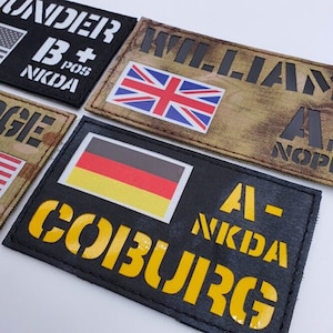 Könnte beinhalten: Vier schwarze und gelbe Militär-Patches mit verschiedenen Flaggen und Text. Die Patches sind aus Stoff gefertigt und haben einen schwarzen Rand. Die Flaggen sind die amerikanische Flagge, die britische Flagge, die deutsche Flagge und die Flagge des Vereinigten Königreichs. Der Text auf den Patches lautet "B+ POS NIKDA", "WILLIAM A- NOP", "A- NIKDA", und "COIBURG".