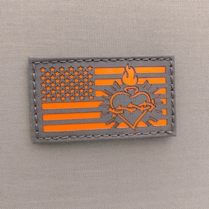 May include: Orange and gray embroidered patch with an American flag design and a stylized heart with flames and thorns. The heart is surrounded by a circle of rays.