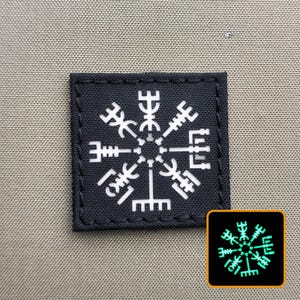 May include: A square, dark gray patch with a white, stylized, radial symbol. The symbol is a variation of the Vegvísir, a Viking compass. A smaller, glowing version of the patch is in the lower right corner. The patch is likely an iron-on or sew-on patch.