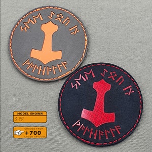 May include: Two round embroidered patches with a hammer symbol and runes. The patch on the left is gray with orange stitching and an orange hammer. The patch on the right is black with red stitching and a red hammer.