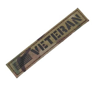 May include: A camouflage fabric patch with the word "VETERAN" in black lettering and a small American flag design.