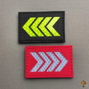 May include: Two rectangular patches with arrow designs. One patch is black with a neon yellow arrow pattern. The other is red with a reflective silver arrow pattern. Both patches have a stitched border.