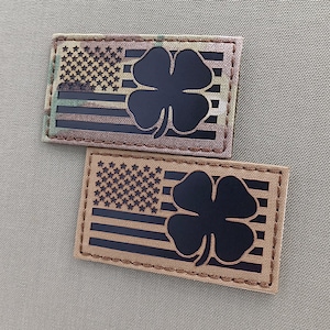 May include: Two brown fabric patches with black embroidered American flags and four-leaf clovers. The top patch has a camouflage pattern.