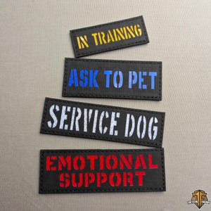 Peut inclure: Quatre écussons rectangulaires noirs avec des coutures blanches. Les écussons portent des inscriptions en jaune, bleu, blanc et rouge : "IN TRAINING", "ASK TO PET", "SERVICE DOG" et "EMOTIONAL SUPPORT". Les écussons sont destinés aux animaux d'assistance.