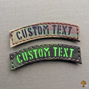 May include: Two custom text patches. One patch features a camouflage pattern with black text, and the other has a black background with green text. Both patches are arched and have stitched borders.