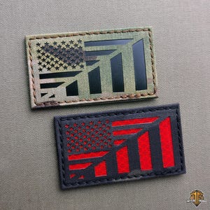 May include: Two rectangular patches with a flag design. One patch features a camouflage background with a black flag design. The other patch has a dark gray background with a red flag design. Both patches have stitched borders.