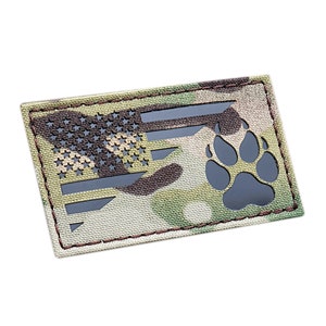 Può includere: Una toppa in tessuto mimetico con un design di bandiera americana e un'impronta di zampa nera. La bandiera è ritagliata per mostrare l'impronta di zampa.