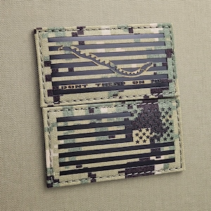 Peut inclure: Un patch en tissu de camouflage noir et vert avec un motif de drapeau américain noir et blanc. Le drapeau a un serpent noir avec un engrenage sur le dessus. Le texte "DON'T TREAD ON ME" est imprimé sur le patch.