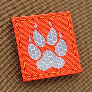 May include: Orange fabric patch with a white reflective paw print. The patch has a yellow stitched border.