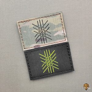 Könnte beinhalten: Zwei rechteckige Aufnäher. Der obere Aufnäher hat ein Tarnmuster mit einem schwarzen geometrischen Design. Der untere Aufnäher ist schwarz mit einem gelben geometrischen Design. Beide Aufnäher haben genähte Kanten.