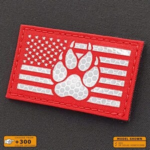May include: Red and white American flag patch with a reflective white paw print in the center. The patch has a red stitched border.