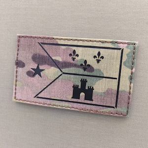 May include: A black and white embroidered patch with the city flag of New Orleans, Louisiana. The patch features a black castle, three fleur-de-lis, and a white star on a camouflage background.
