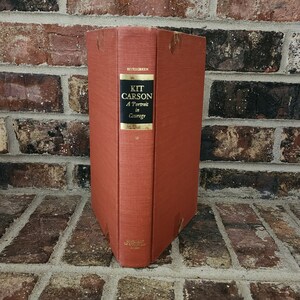 May include: A red hardcover book titled "Kit Carson: A Portrait in Courage" by  Evergreen.