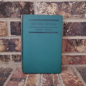 May include: A green hardcover book with the title "THE HILLS BEYOND" and the author "THOMAS WOLFE" printed on the front cover.