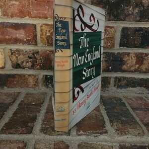 May include: A vintage hardcover book titled "The New England Story" by Henry Beetle Hough. The book cover features a green and white striped design with a stylized ampersand symbol.