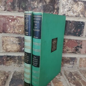 May include: Two vintage hardcover books with green covers. The book on the left has a gold spine with the title "Moratin's La Comedia Nueva and El Si de las Ninas" by Humphrey Wilson. The book on the right has a black spine with the title "Monteros' Puebla de las Mujeres" by Adams. Both books are part of "The Century Modern Language Series."