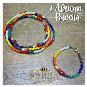 May include: A colorful beaded necklace and bracelet set with red, orange, yellow, green, blue, white, and purple beads. The necklace is layered and the bracelet has a gold clasp. The text "7 African Powers" is written in black above the set and "OSHUN SQUARED" is written below the set.