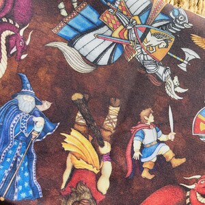 May include: A brown fabric featuring a fantasy scene with dragons, knights, and wizards. The design includes a red dragon, a blue-robed wizard, and a knight in armor. The fabric has a detailed, illustrated style.