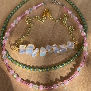 May include: Three layered necklaces with a gold chain, pink and green beads, and a bar of opal stones.