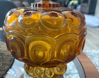 May include: A vintage amber glass candy dish with a domed lid and a decorative knob. The dish has a textured surface with a repeating pattern of circles and stars.
