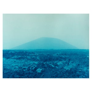 May include: A blue and white landscape photograph of a mountain range in the distance, with a foreground of rough, rocky terrain.