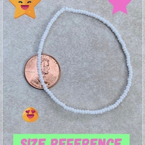 May include: A white beaded bracelet next to a US penny for size reference. The bracelet is made of small, round beads.