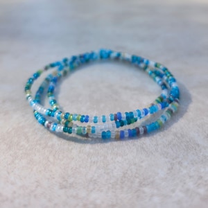 May include: A multi-strand bracelet made of small, colorful glass beads. The beads are in shades of blue, green, and white.