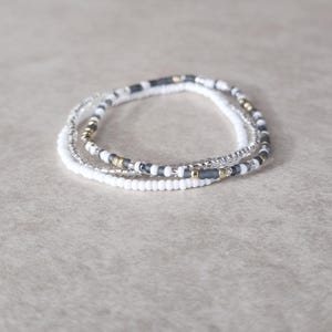 May include: Three layered bracelets with white, gray, and gold beads.