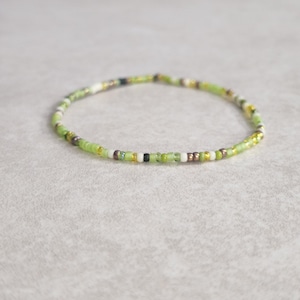 May include: A delicate green, white, and gold beaded bracelet. The bracelet is made with small, colorful beads and has a simple, elegant design.