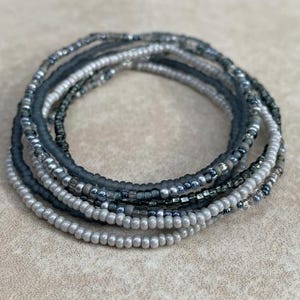 May include: A set of layered bracelets made with gray and silver beads. The bracelets are stacked on top of each other, creating a layered look.