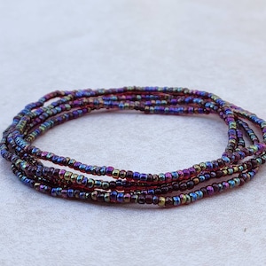 May include: A multi-strand beaded bracelet with iridescent beads in shades of purple, red, and gold.