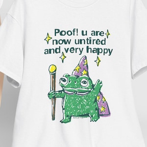 Puede incluir: Camiseta blanca con un dibujo de una rana mago sosteniendo un bastón. La rana lleva un sombrero de mago morado y amarillo. El texto en la camiseta dice "Poof! u are now untired and very happy."