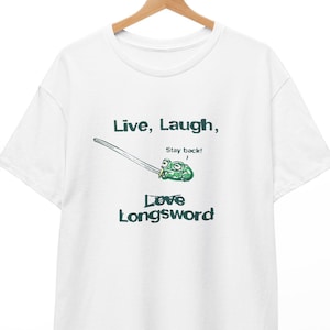 May include: White t-shirt with the text "Live, Laugh, Love Longsword" in green. A cartoon illustration of a longsword with a frog is featured above the text. The shirt is hanging on a wooden hanger.
